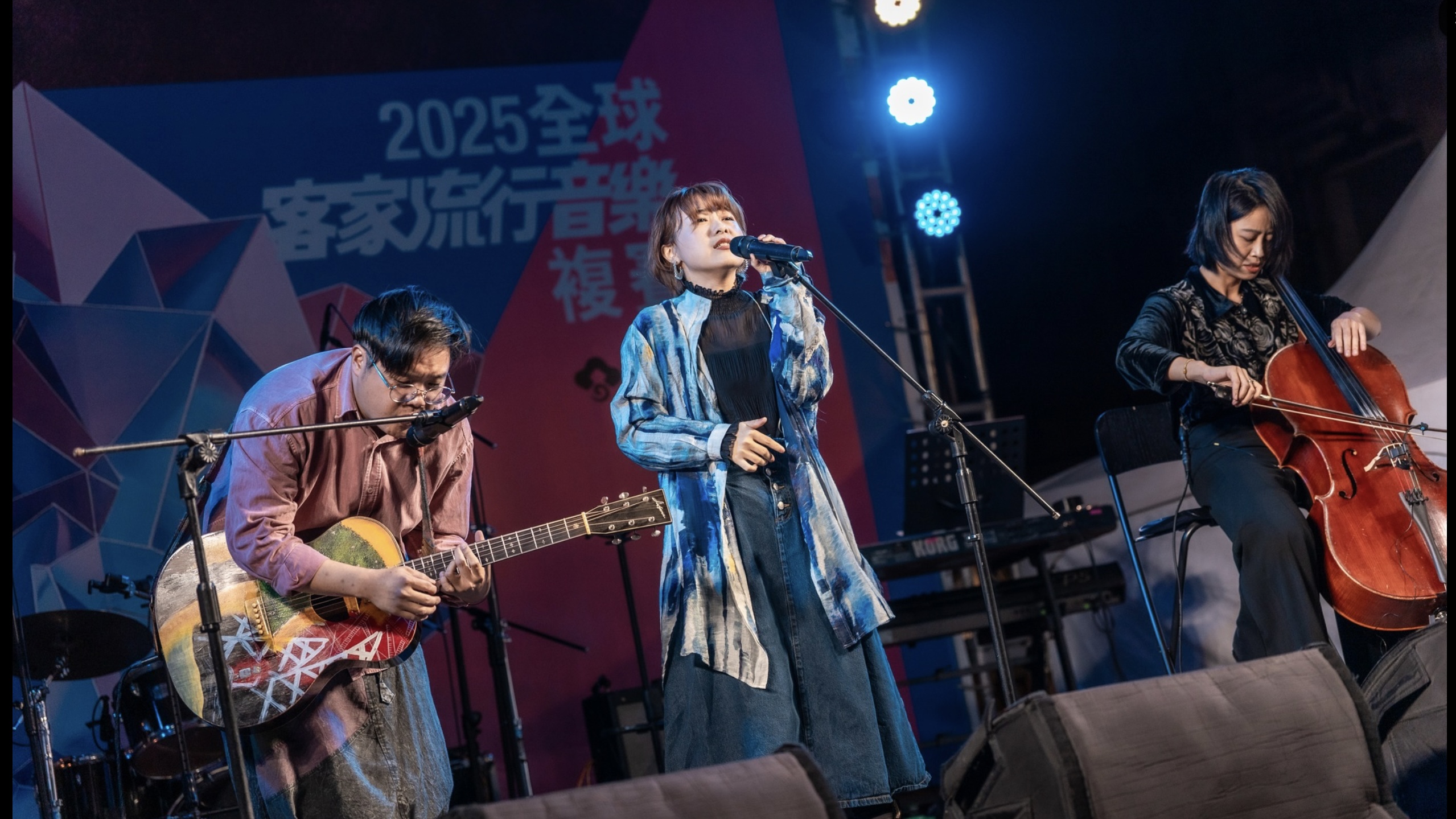 三人樂團正在「2025全球客家流行音樂」的舞台上投入地進行現場演出