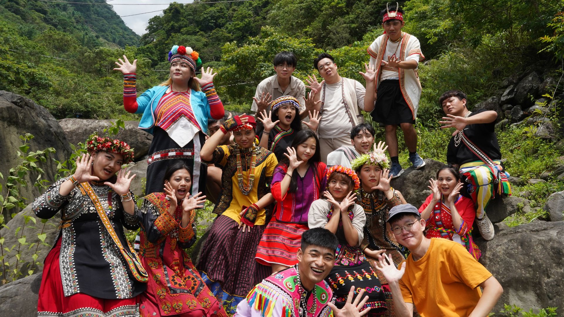 一群年輕人身處在綠意盎然、怪石嶙峋的溪谷山林背景中，張開雙手擺出開朗、活潑的姿勢。