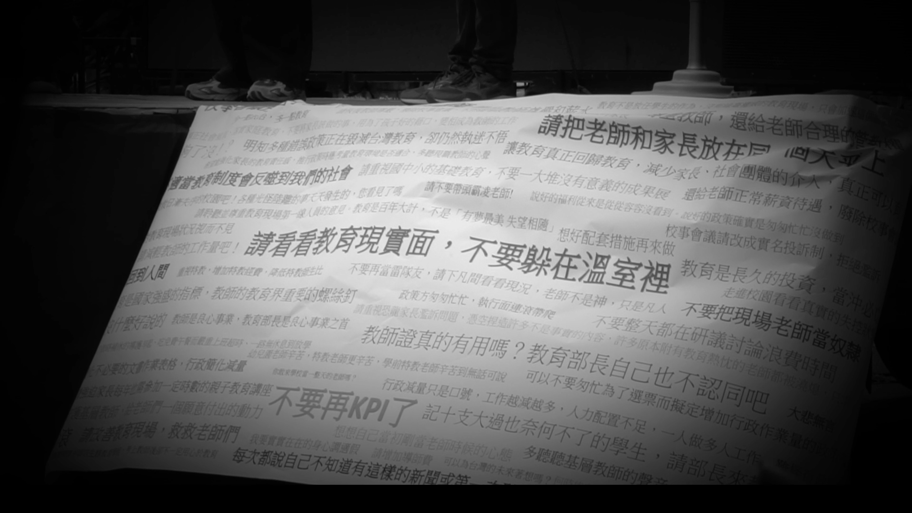 透過鋪滿抗議標語的巨大布條，沉痛傳達了基層教師對教育體制與現況的強烈控訴。