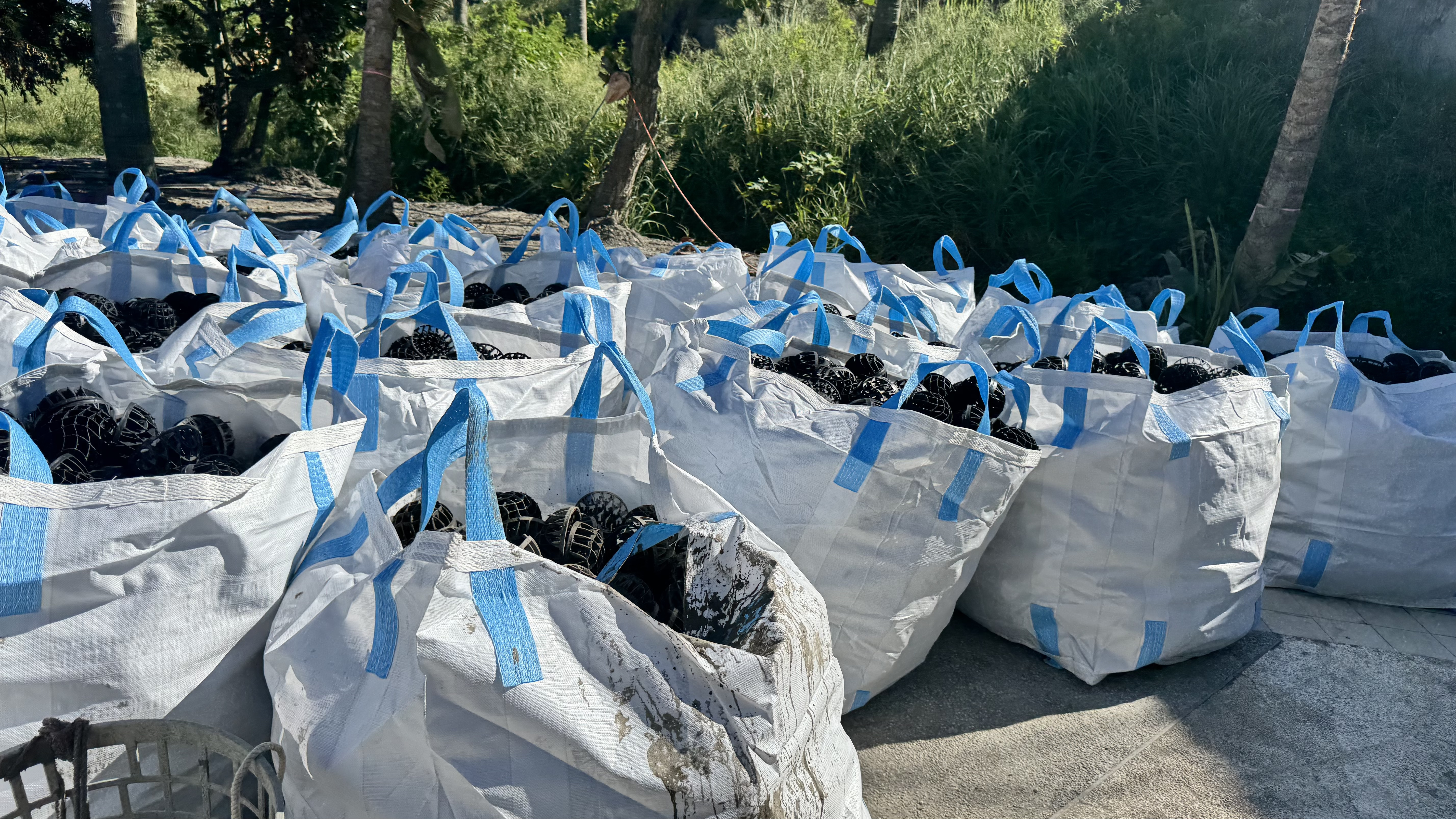 許多大型白色編織袋，裡面裝滿黑色的塑膠結構物