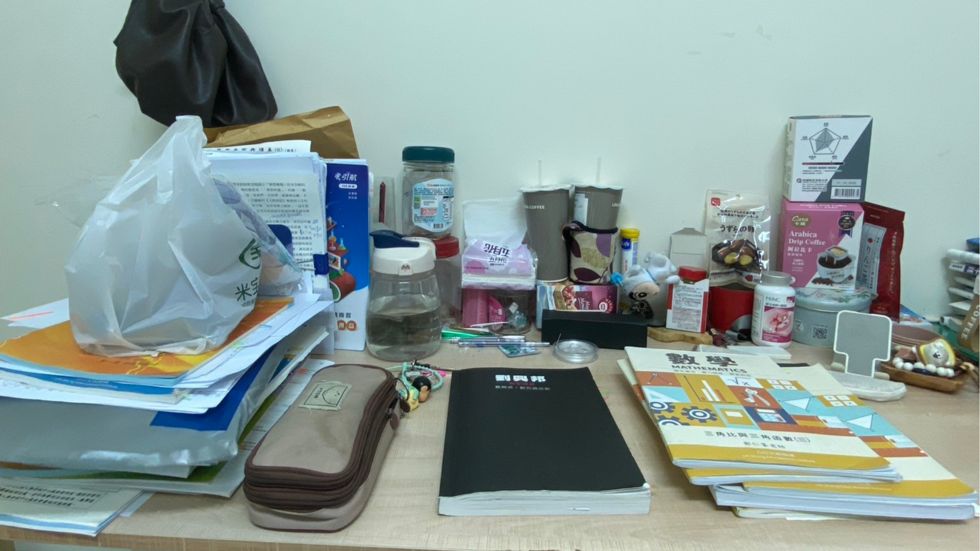 書桌上擺放許多書本、考卷、筆袋與各種生活用品