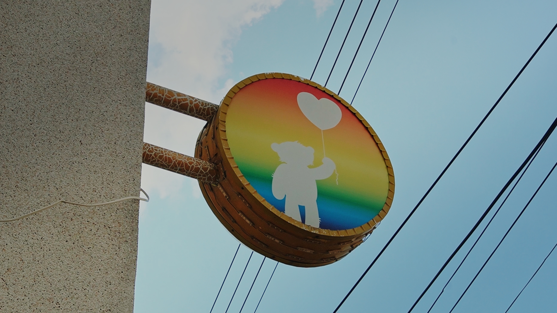 上面有一隻熊拿著一個愛心氣球,背景是彩虹色的圓形招牌