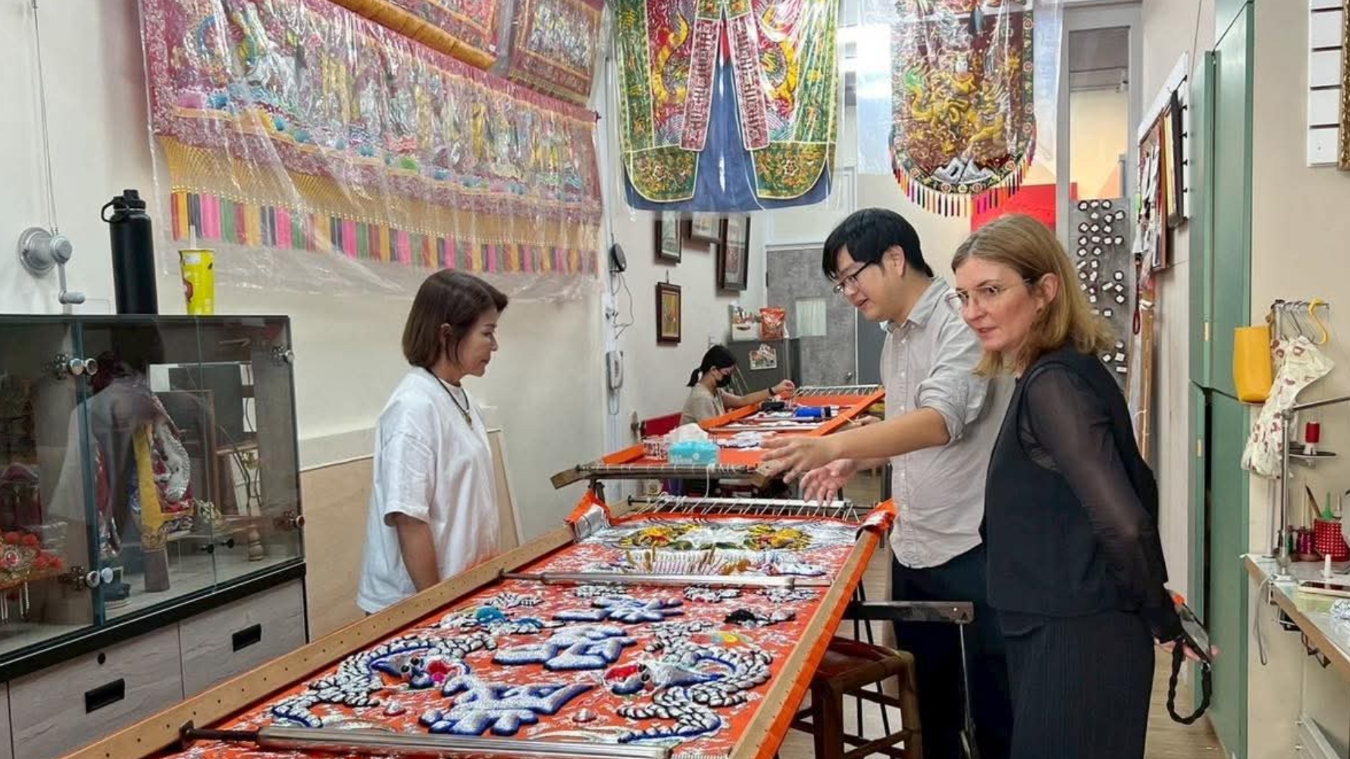一家傳統刺繡工坊內，導覽人員正向外籍訪客介紹繃在大型木架上、圖案精美的傳統宗教立體刺繡作品。