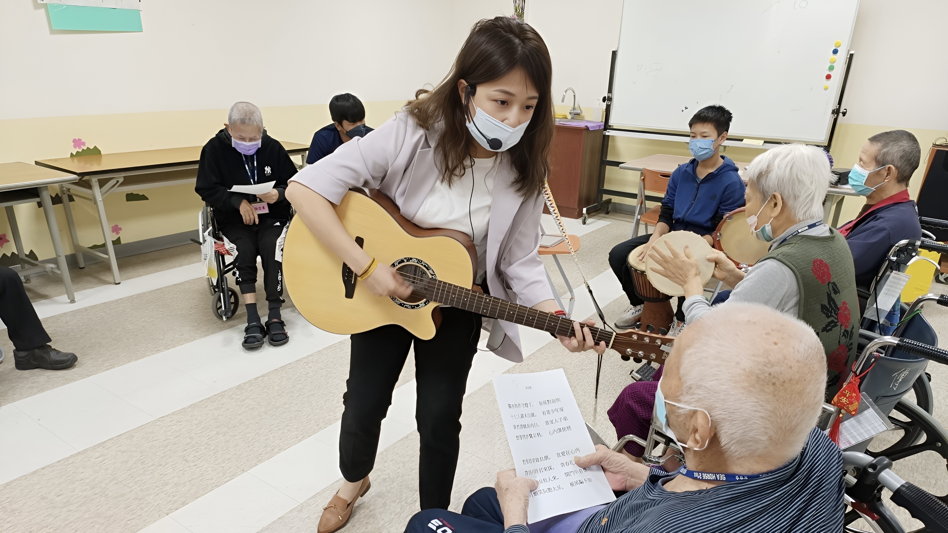 治療師正在對一名長者彈吉他，教室內坐著數名失智症患者