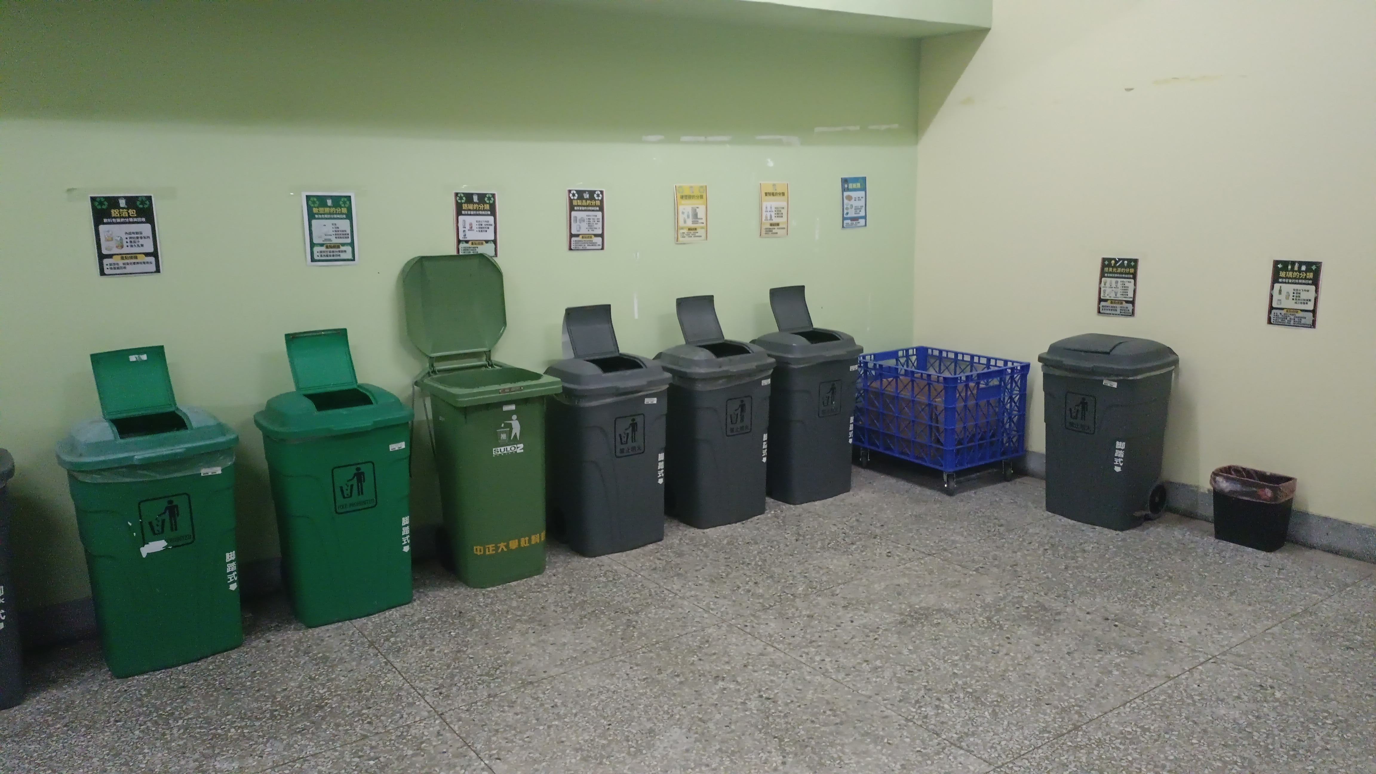 牆上貼有各類分類告示,並對應擺放多個綠色與灰色的分類垃圾桶。