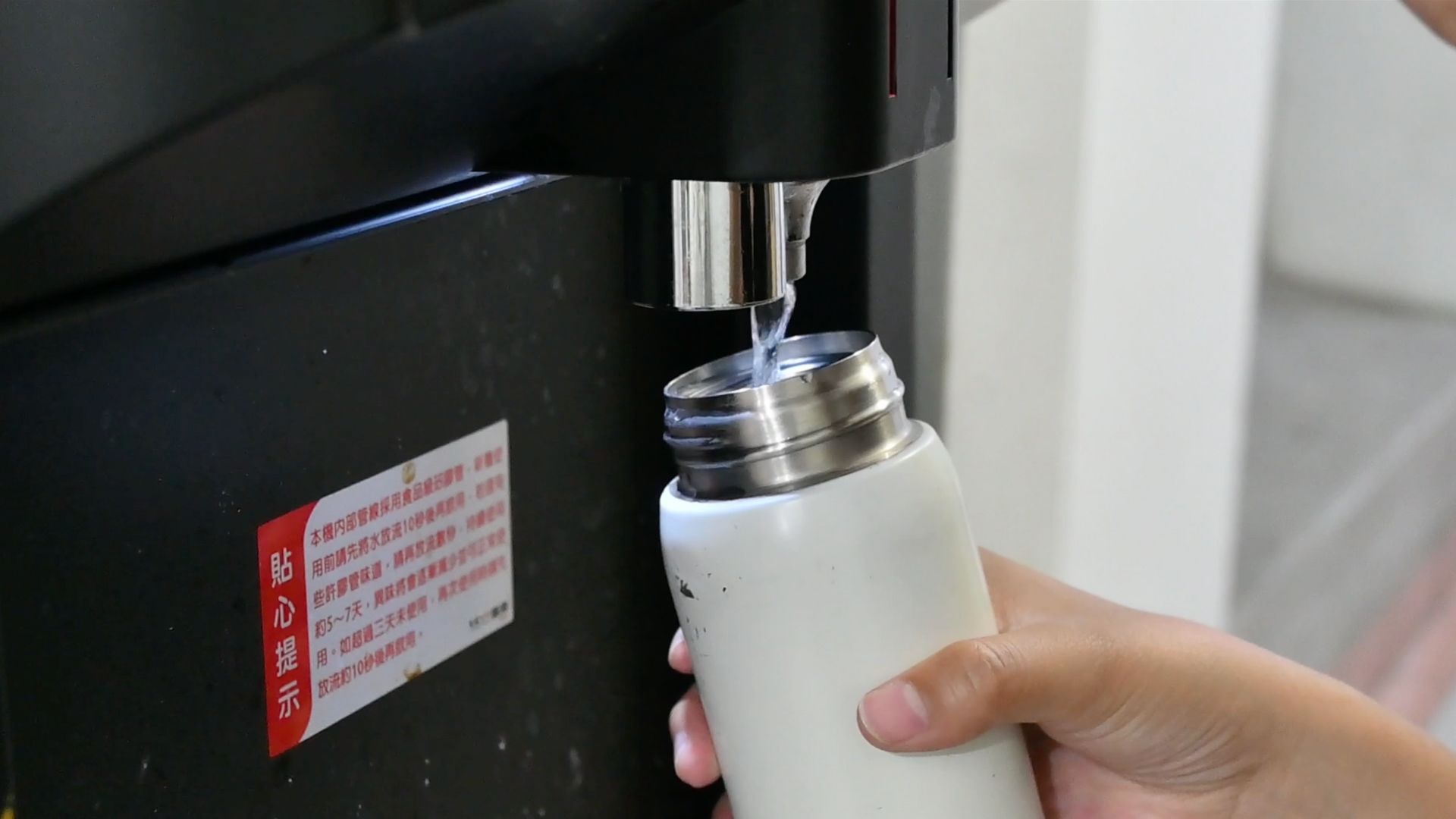 一隻手拿著一個白色水壺正在飲水機裝水