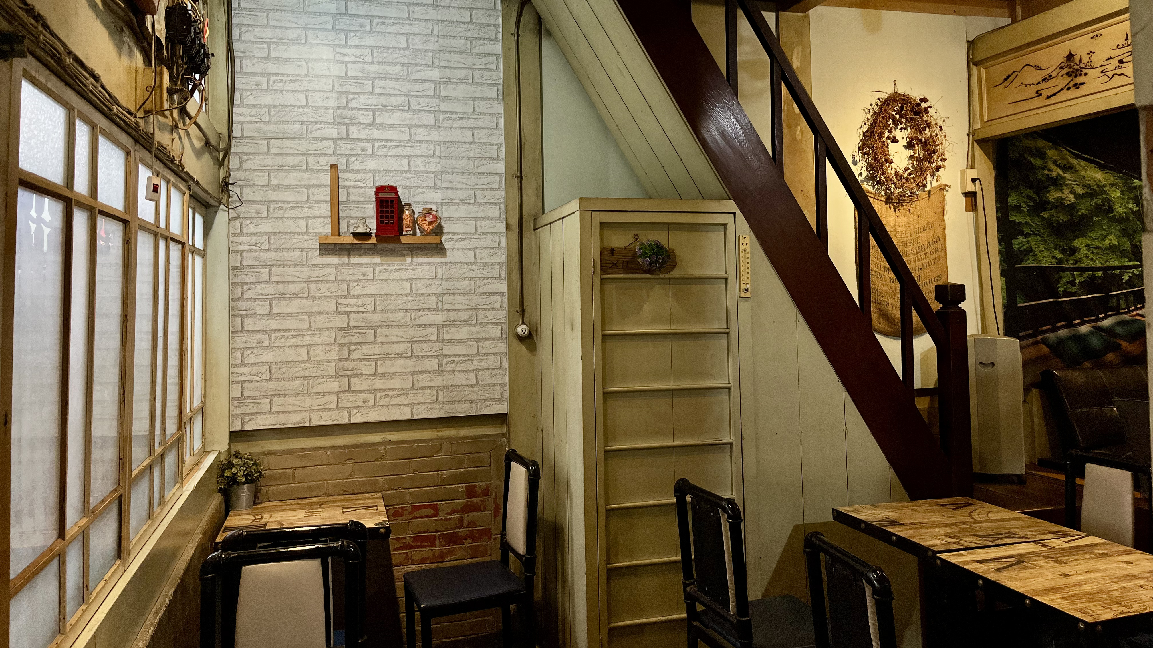 懷舊風格的室內空間，木質階梯旁設有簡單的桌椅，白磚牆上點綴著紅色電話亭裝飾，營造出溫馨靜謐的氛圍。
