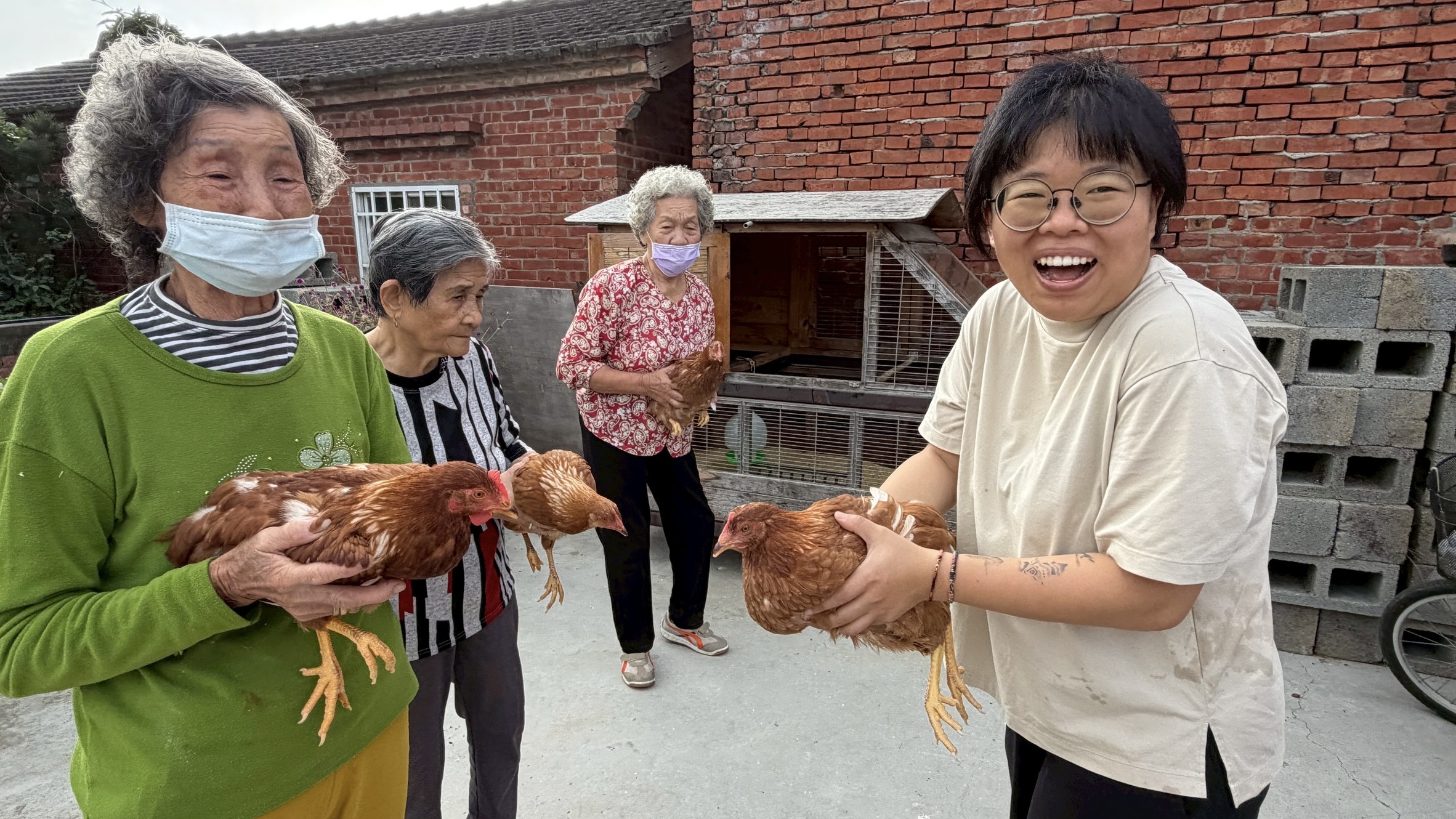 長輩與年輕人在紅磚平房前共同抱著雞隻。
