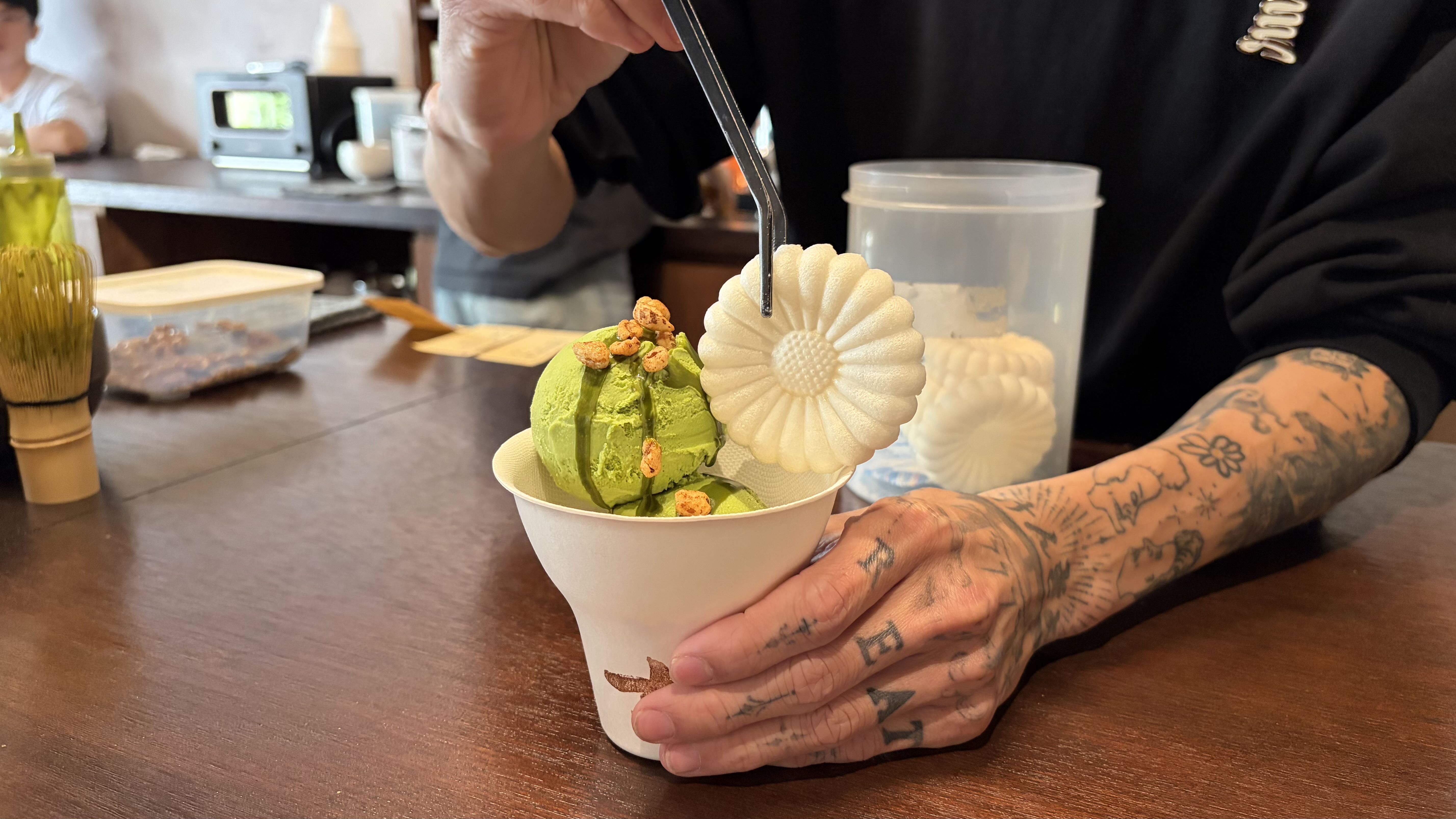 一隻手拿著一個裝有抹茶冰淇淋與菊花造型餅乾的白色杯子