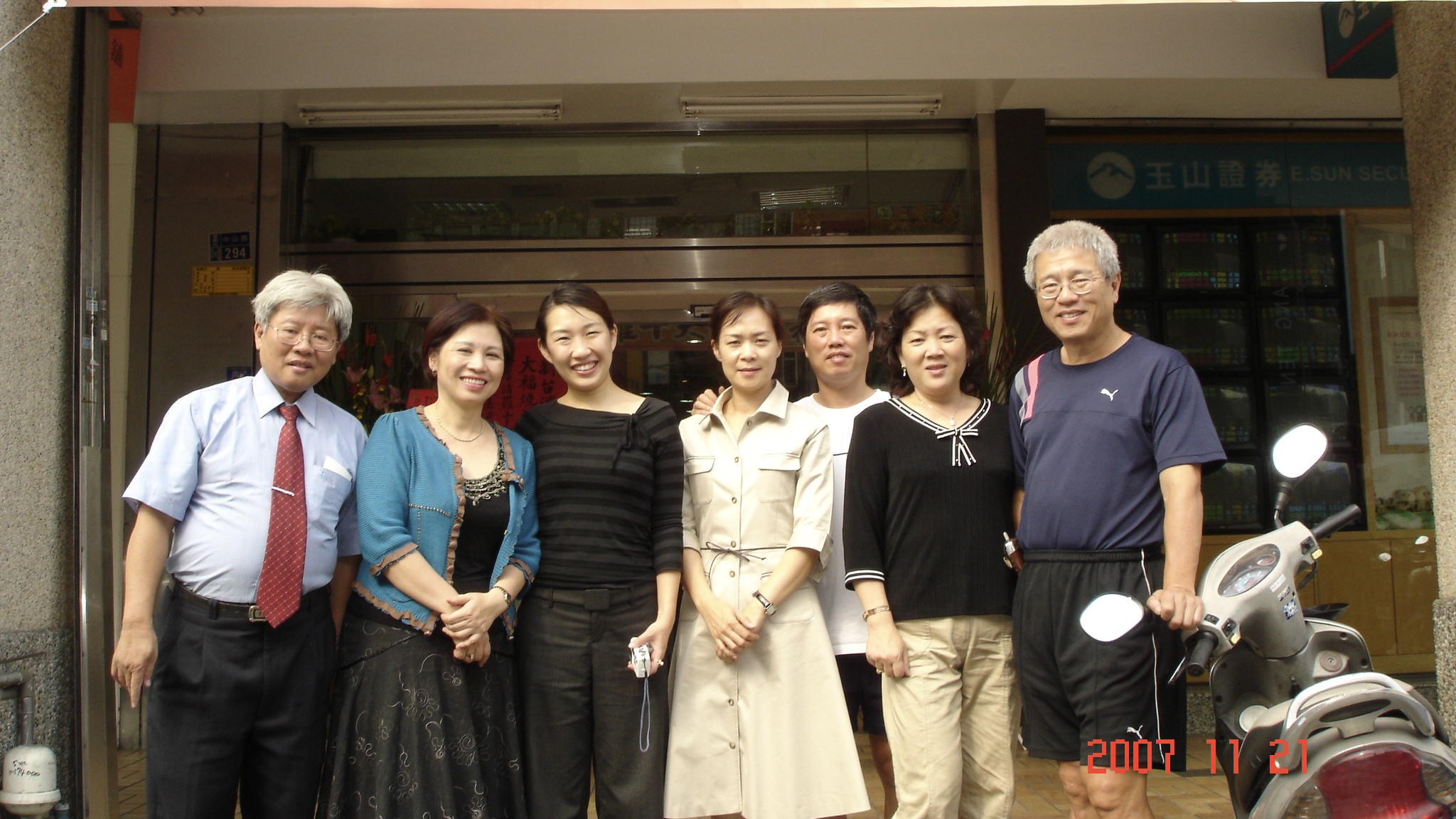 這是一張攝於 2007 年 11 月 21 日的生活合照，畫面中有三男四女在店面門口合影留念。