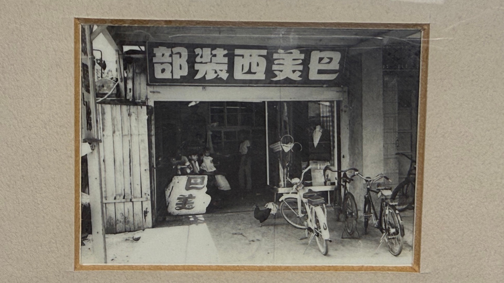 這是一張懷舊的黑白老照片，畫面中是「巴美西裝部」的店面外觀，門口停放著幾輛舊式腳踏車。