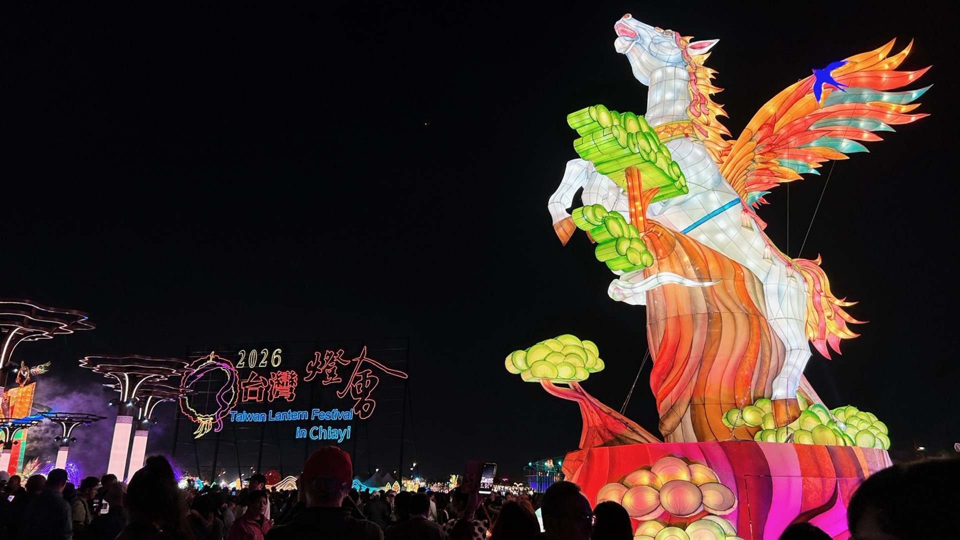 夜空中矗立著一座巨大的天馬主燈，背景可見「2026 台灣燈會」的霓虹字樣與觀賞的人潮。