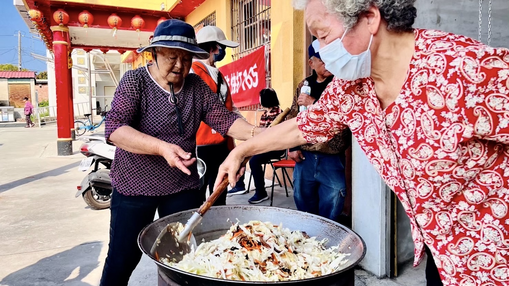 長輩們在戶外使用大鍋熱情翻炒菜餚。