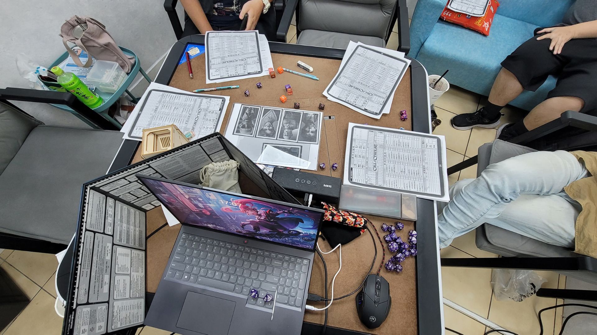 一組人正在進行桌上角色扮演遊戲（TRPG），桌面上擺滿了角色卡、多面骰、筆記型電腦及遊戲主持人的遮板。