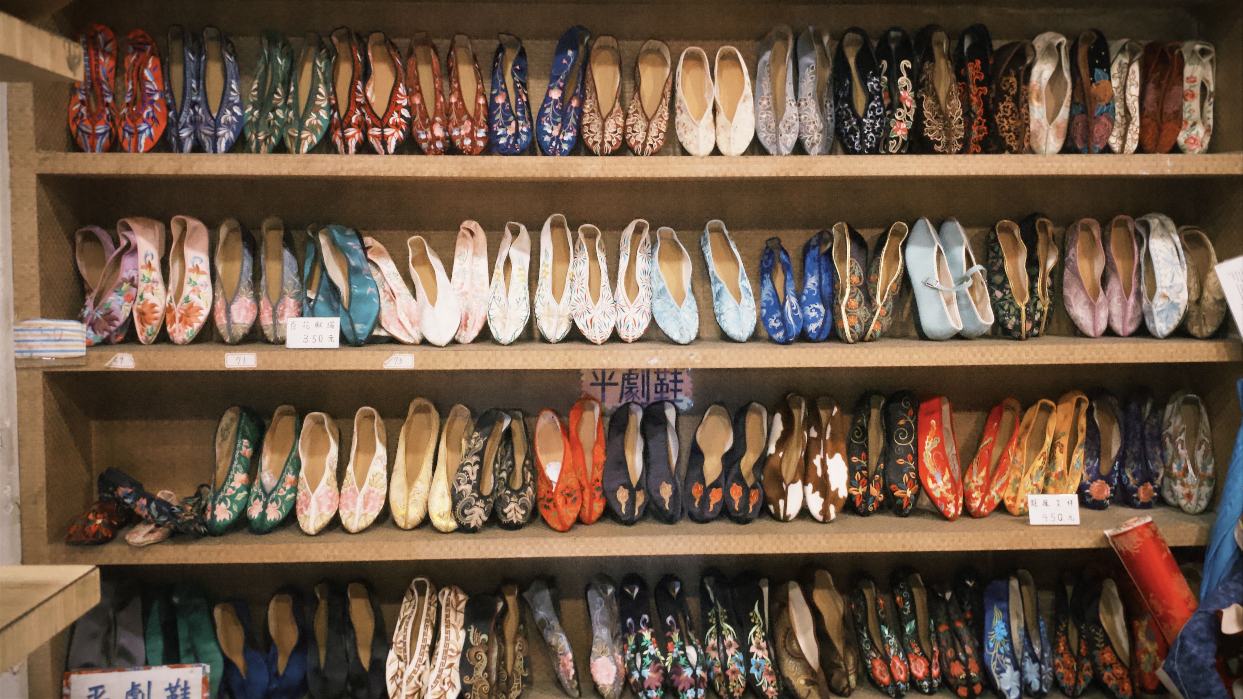 牆面上共四層的層架上展示著不同花色的繡花鞋