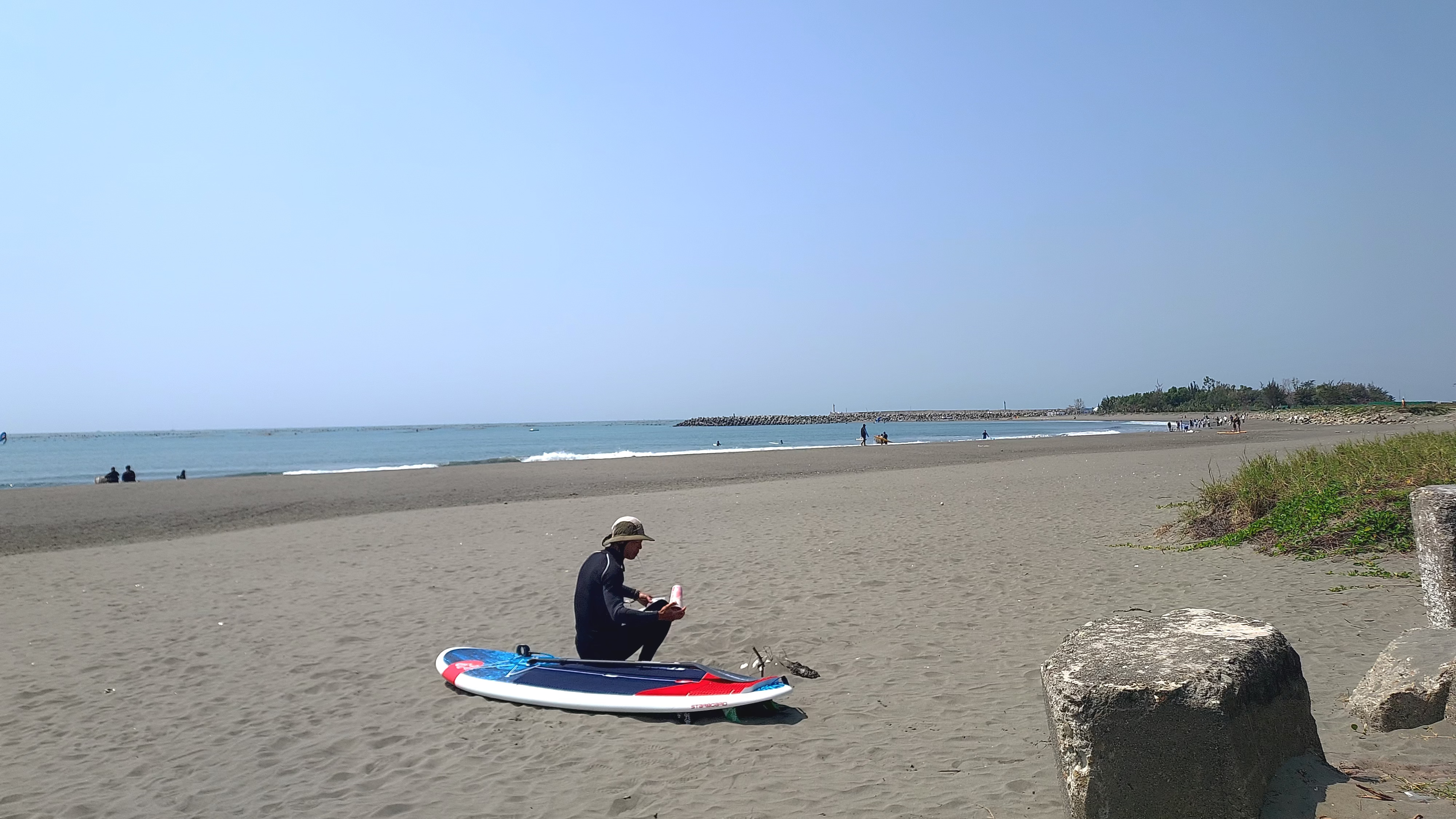 沙灘上有一位民眾穿著潛水服坐在衝浪板上