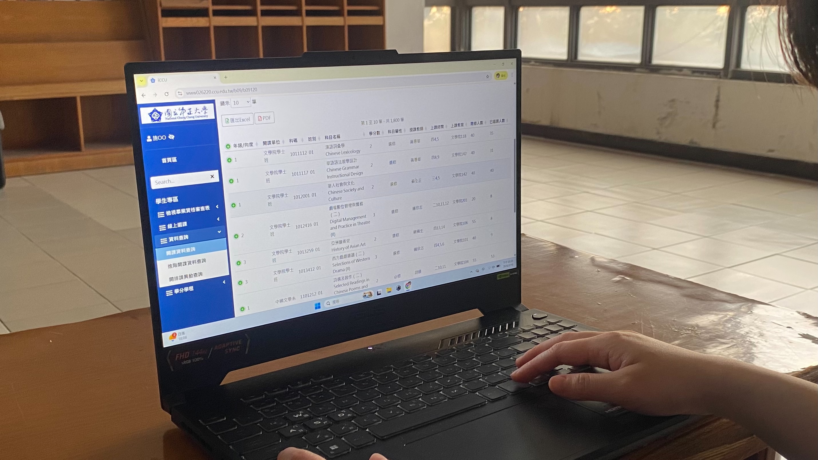 一名學生正在操作筆記型電腦，螢幕上顯示著中正大學新版選課系統的開課資料查詢頁面。