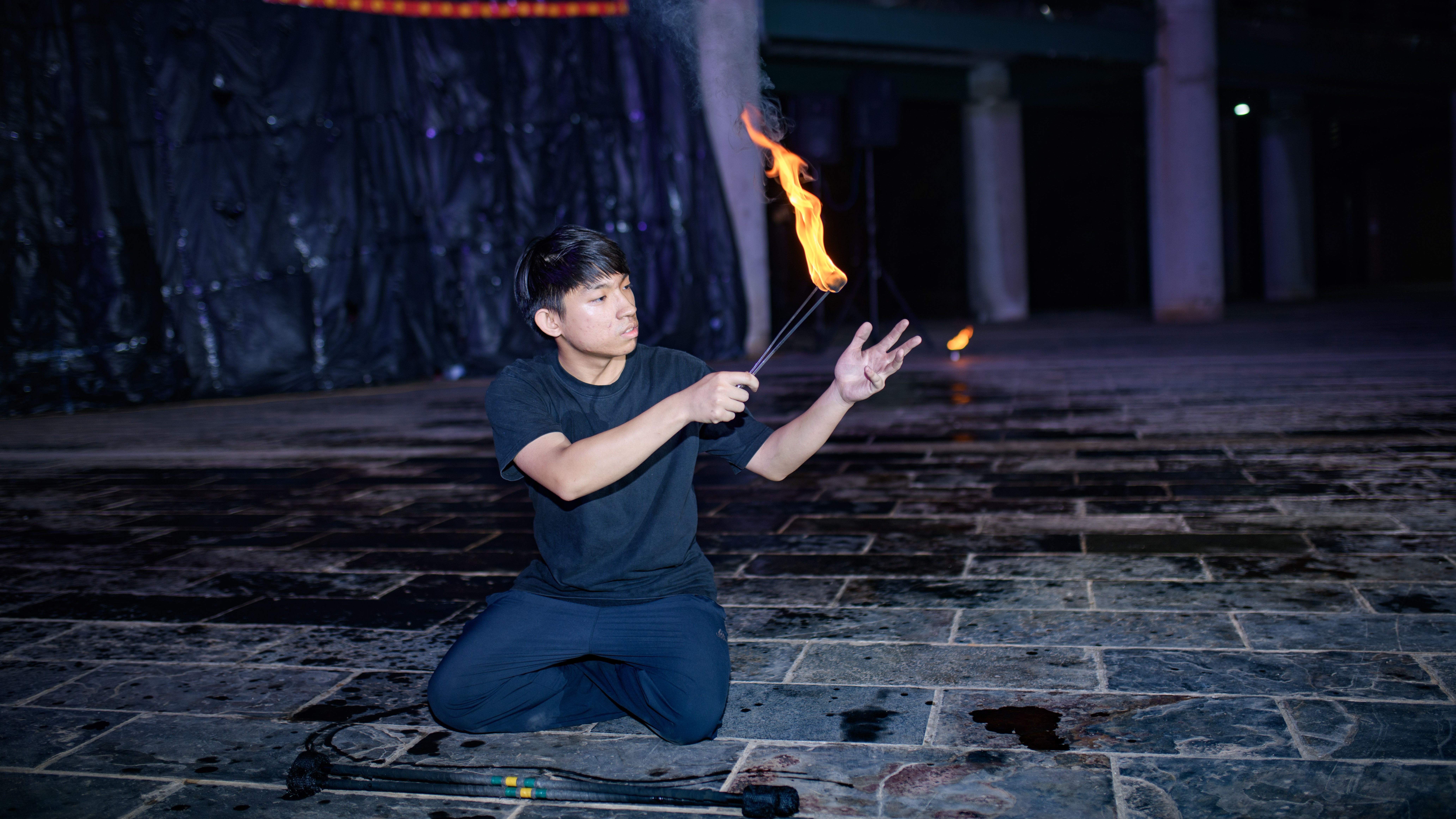 陳霆峻跪坐在地上，手上的夾子夾著一顆燃燒的火球