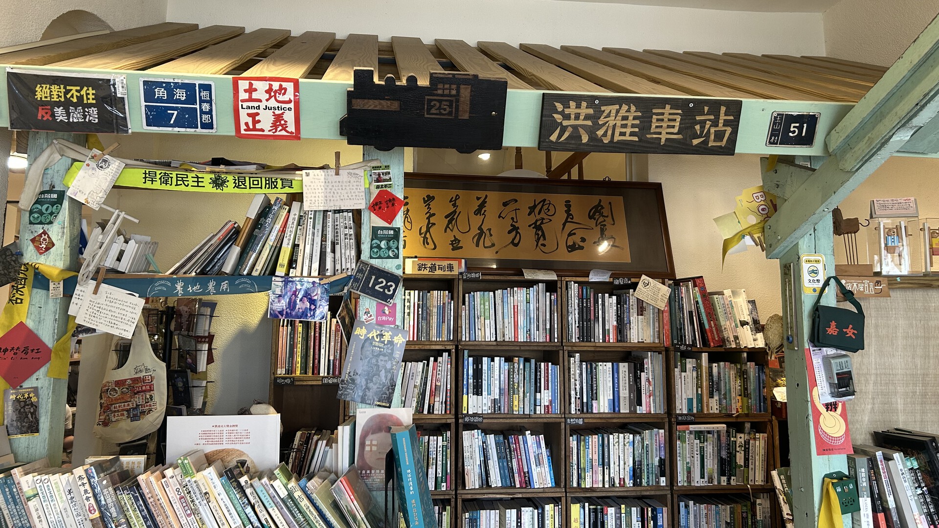 書架上擺滿各類書籍，牆上掛著書寫作品與各式手寫標語、布條、貼紙裝飾