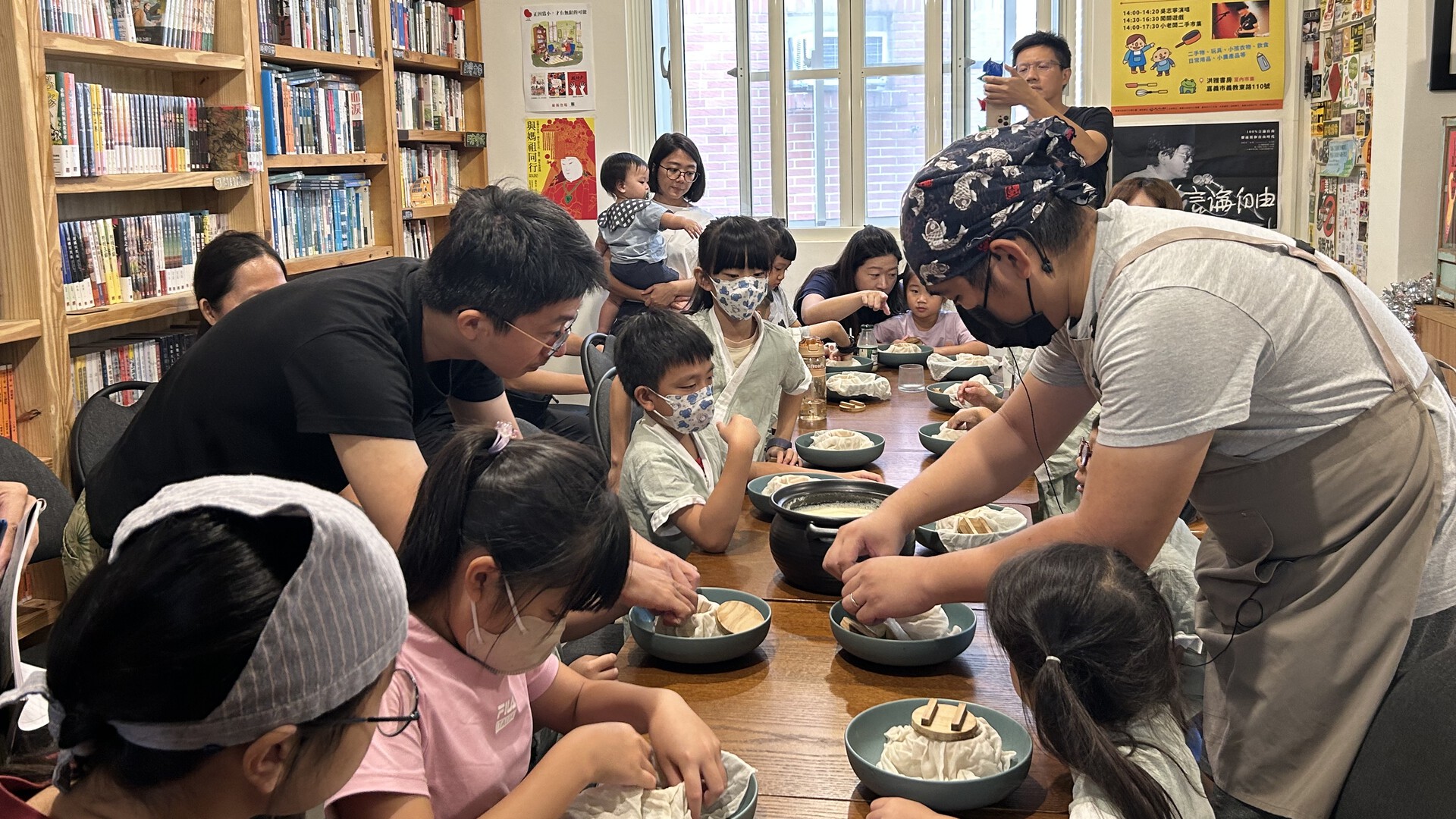 長桌邊坐滿製作豆花豆腐的孩童與家長，老師正在示範如何製作