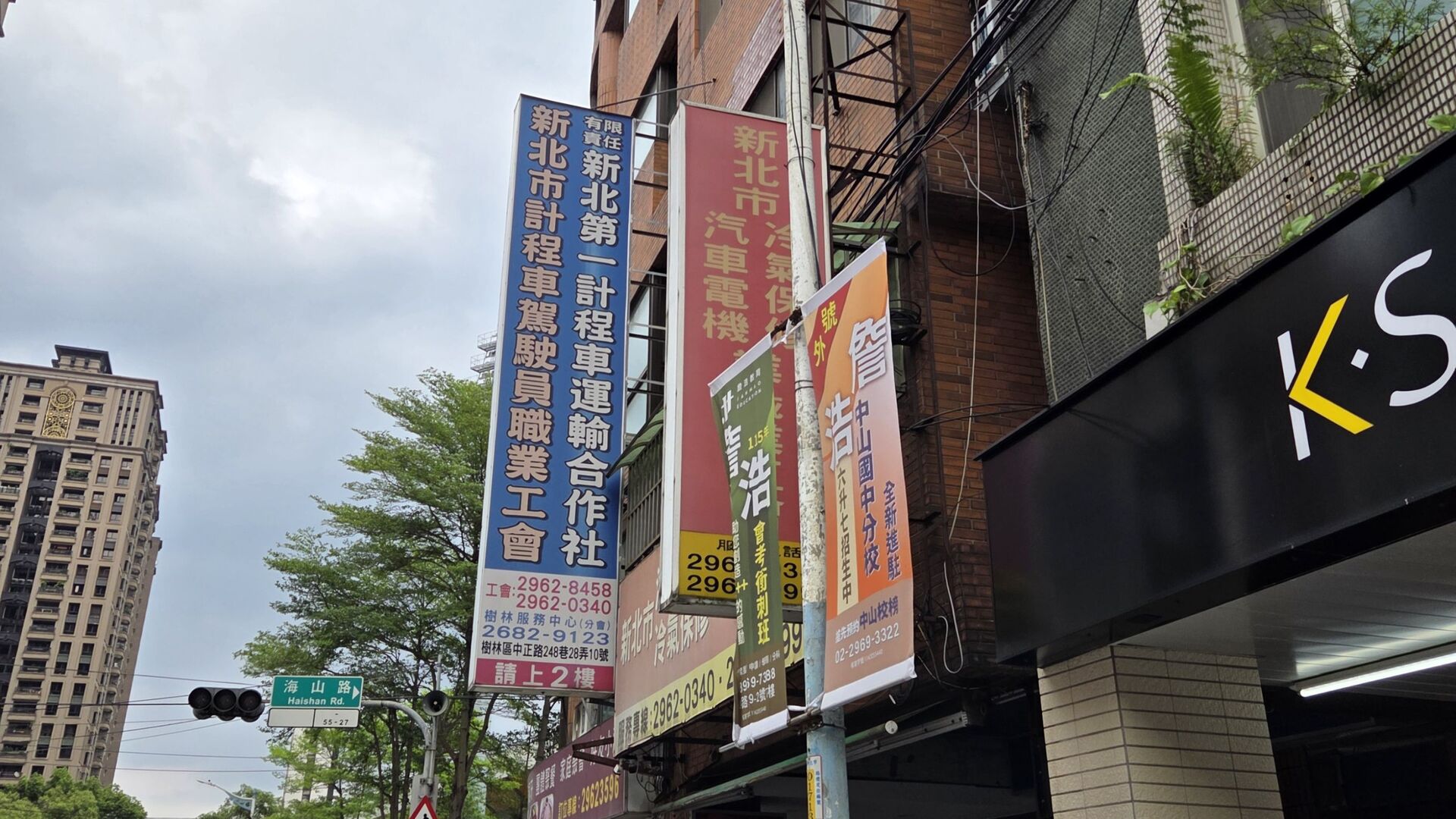街道旁的建築外牆掛著「新北市計程車駕駛員職業工會」與「有限責任新北市第一計程車運輸合作社」的藍色長型招牌。