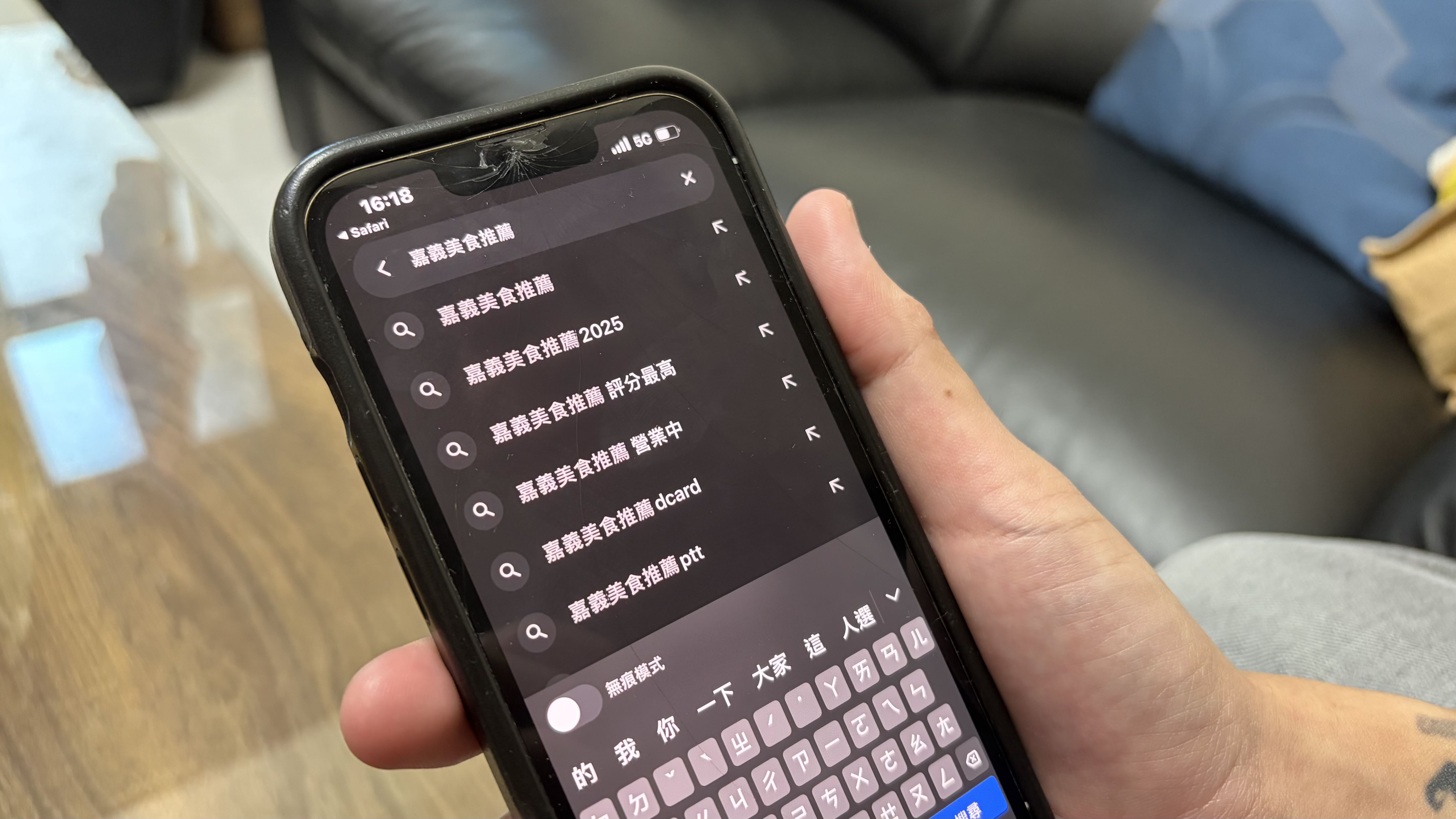 一隻手拿著一支手機，手機畫面是「嘉義美食推薦」的搜尋建議頁面