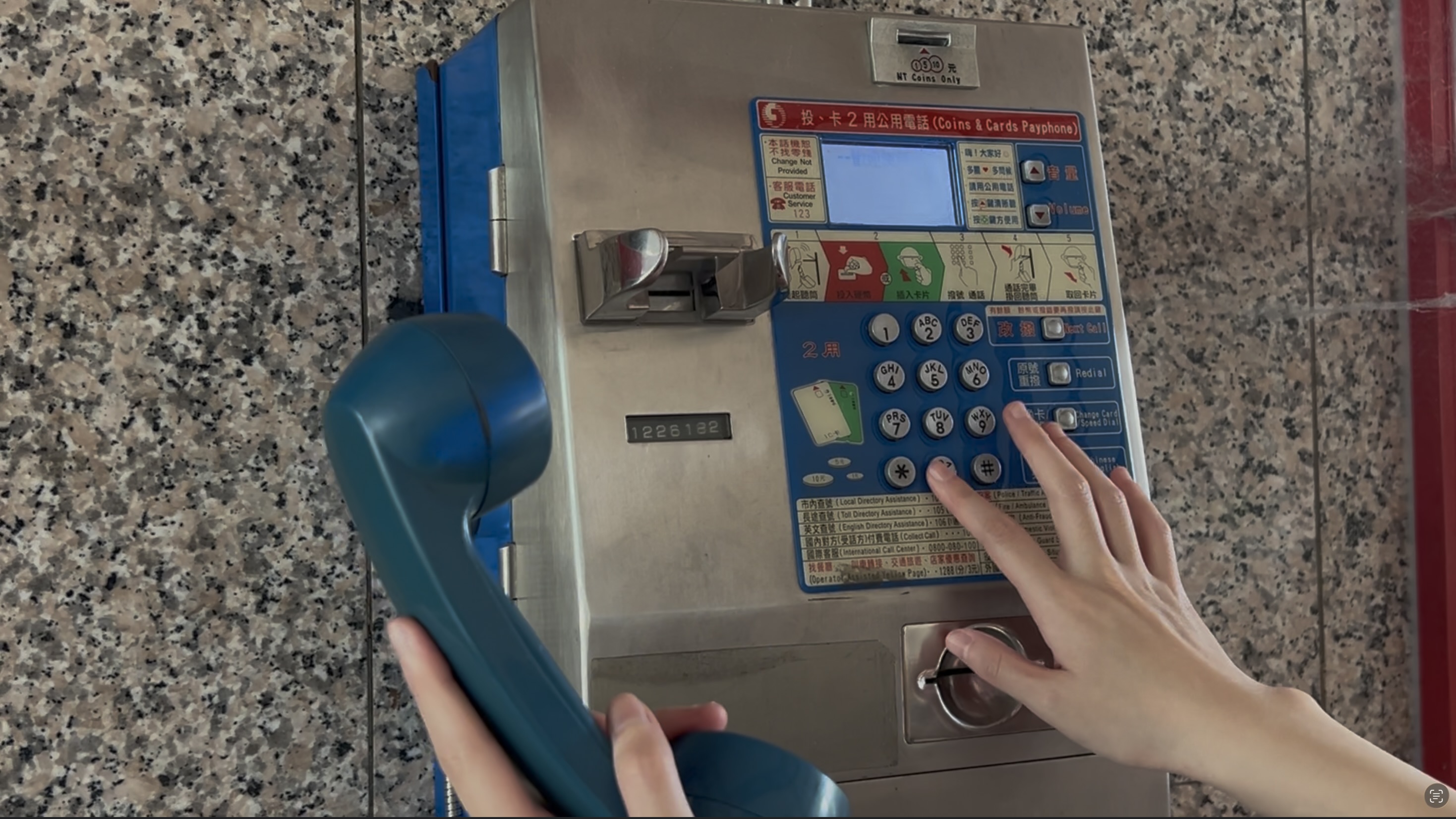 一人右手拿著藍色公共電話聽筒，左手正按下撥號按鈕。