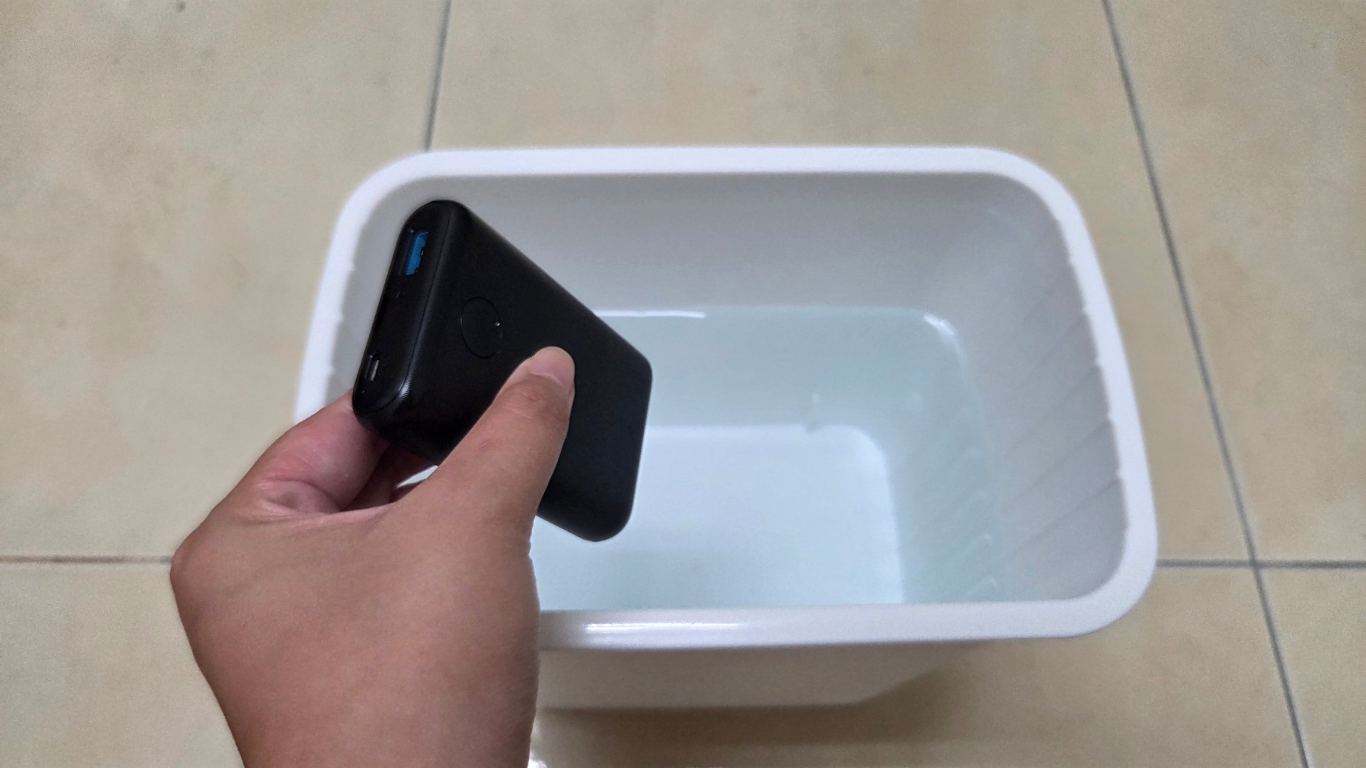 一隻手拿著一顆行動電源在一桶水上方