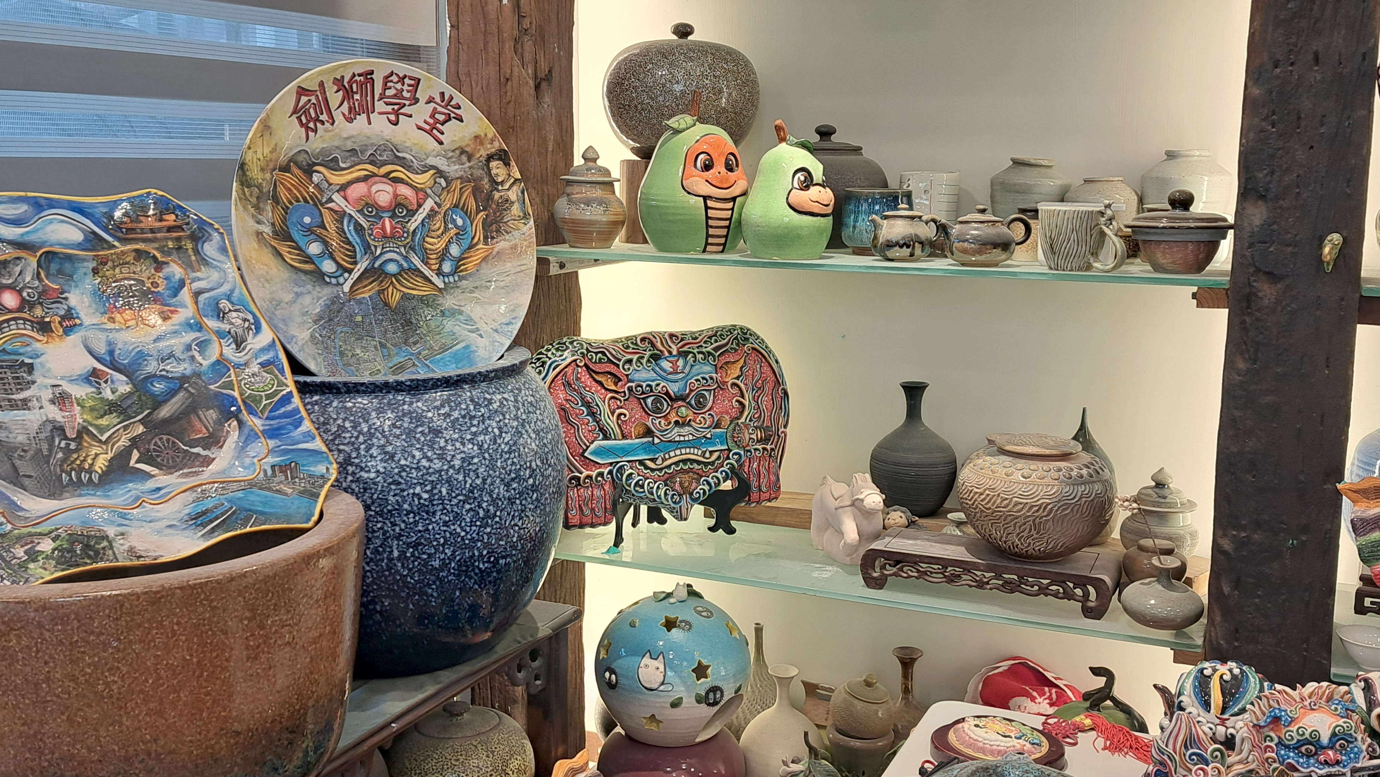 展示架上陳列著多樣化的陶藝作品,左上方寫有「劍獅學堂」的彩繪瓷盤。