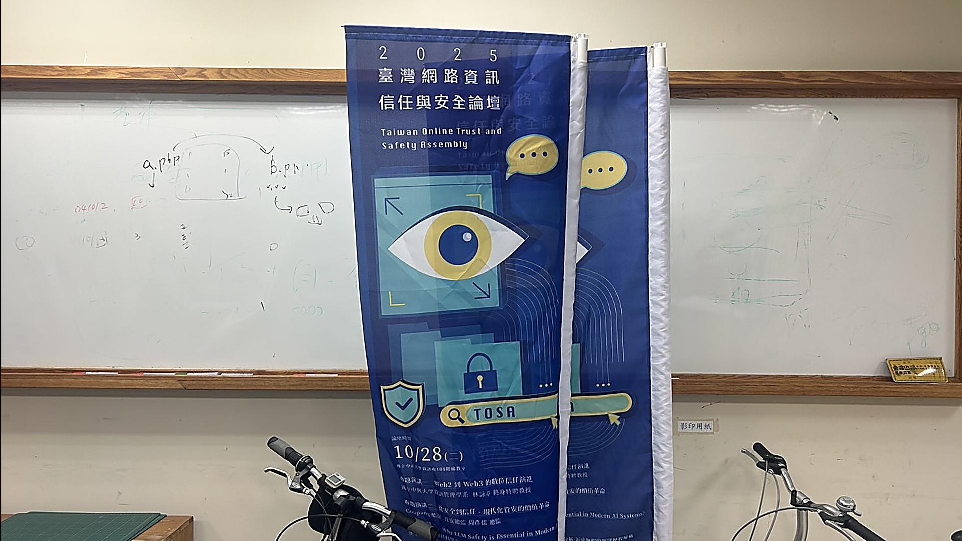在白板牆前方,放置著「2025 臺灣網路資訊信任與安全論壇」的活動宣傳旗幟,內容提及數位信任、現代化資安等議題。