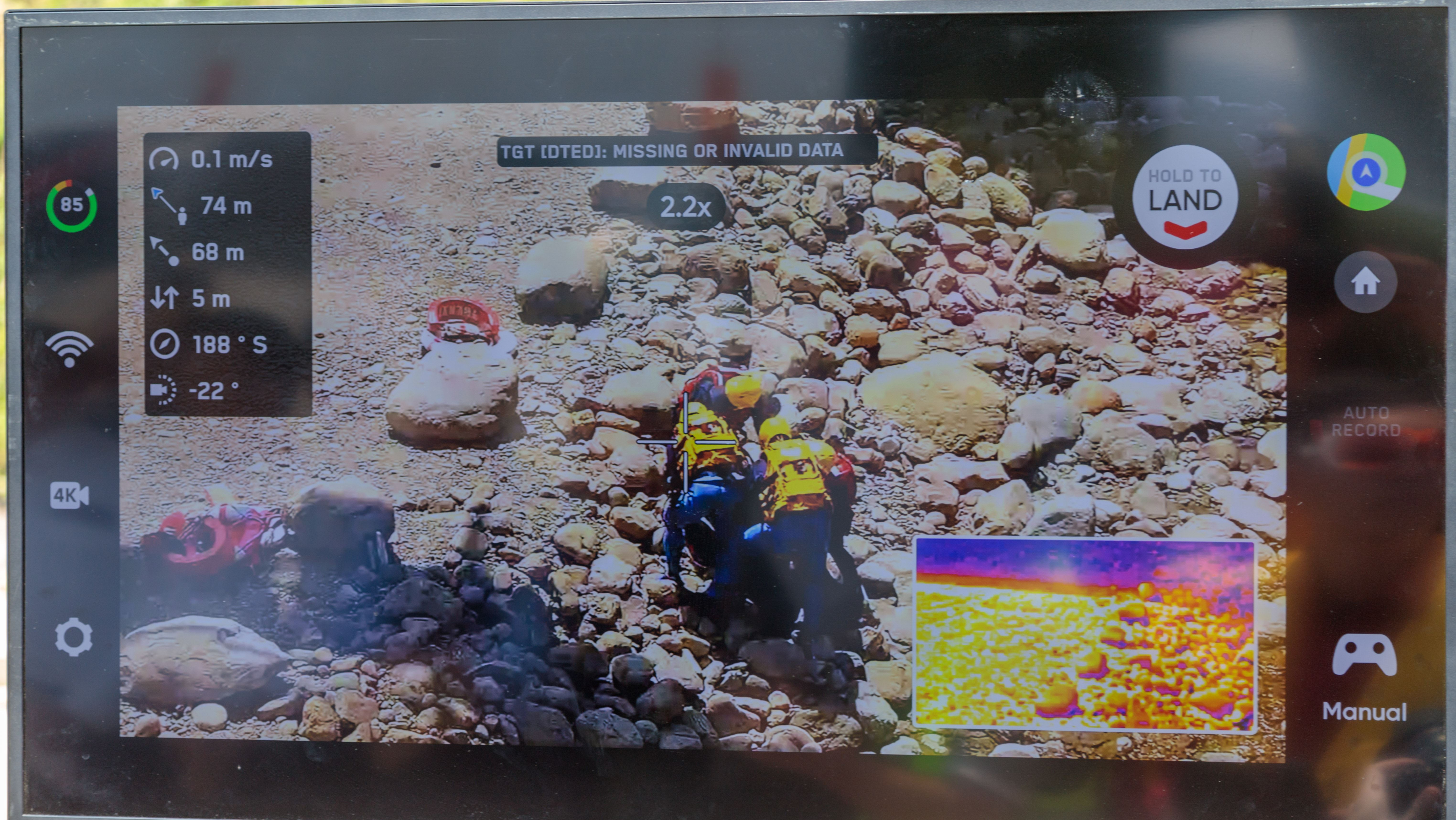 螢幕中央可見幾名穿著藍色搜救服與黃色頭盔的救援人員，正聚集在佈滿岩石的河床或荒地進行任務。