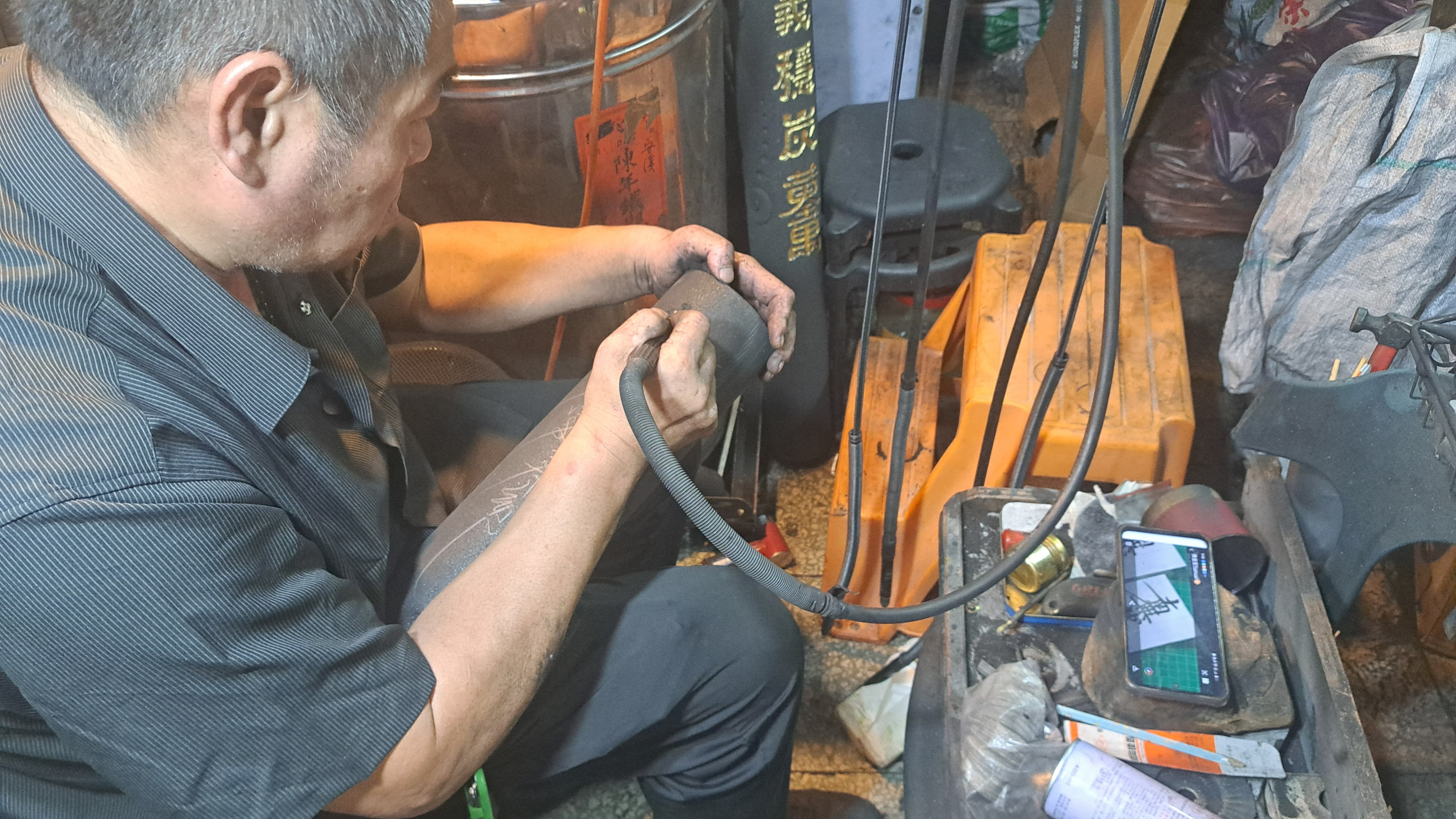 一位年長的工匠，正專注地在工作室內進行木炭雕刻作業。