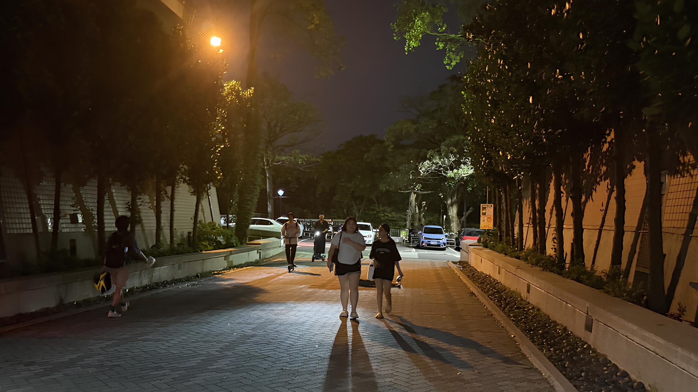 夜間的校園有幾名學生正步行或騎乘電動滑板車經過。