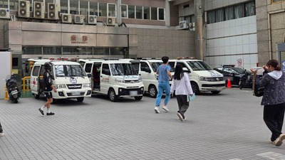 一家醫院的急診室入口外停放著多輛救護車，現場有醫護人員與民眾正在走動。