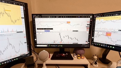 三螢幕的電腦工作桌，畫面上正開啟著加密貨幣交易平台的K線圖與走勢分析圖表。