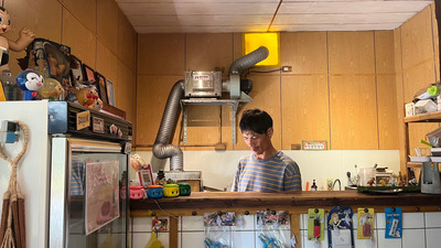 老闆在店裡工作,店內的冰箱與櫃檯上擺放著許多公仔與玩偶