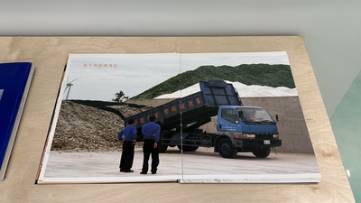 一本攤開平放在淺色木質桌面上的書本，旁邊還疊放著另一本深藍色的書。