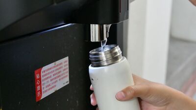 一隻手拿著一個白色水壺正在飲水機裝水