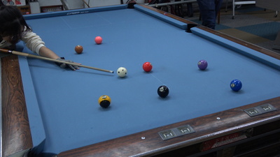 撞球桌邊有一個人拿著撞球桿瞄準球