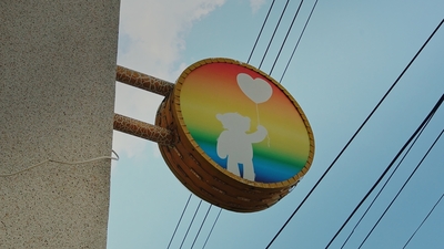 上面有一隻熊拿著一個愛心氣球，背景是彩虹色的圓形招牌