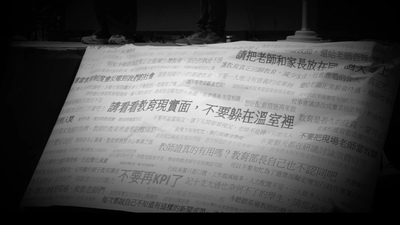 透過鋪滿抗議標語的巨大布條，沉痛傳達了基層教師對教育體制與現況的強烈控訴。